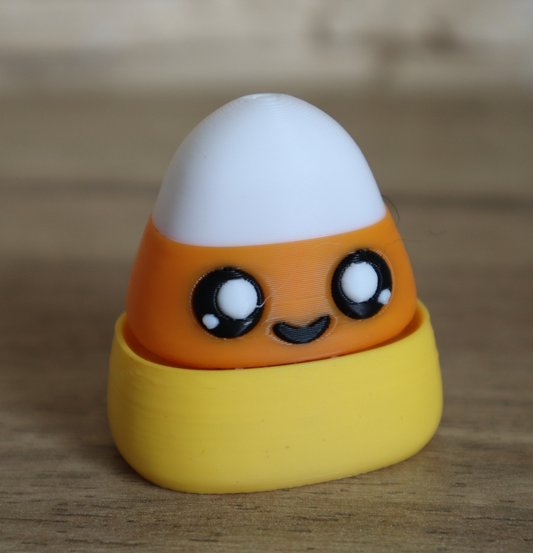A cute, 3D-printed candy corn clicker toy with a smiling face.