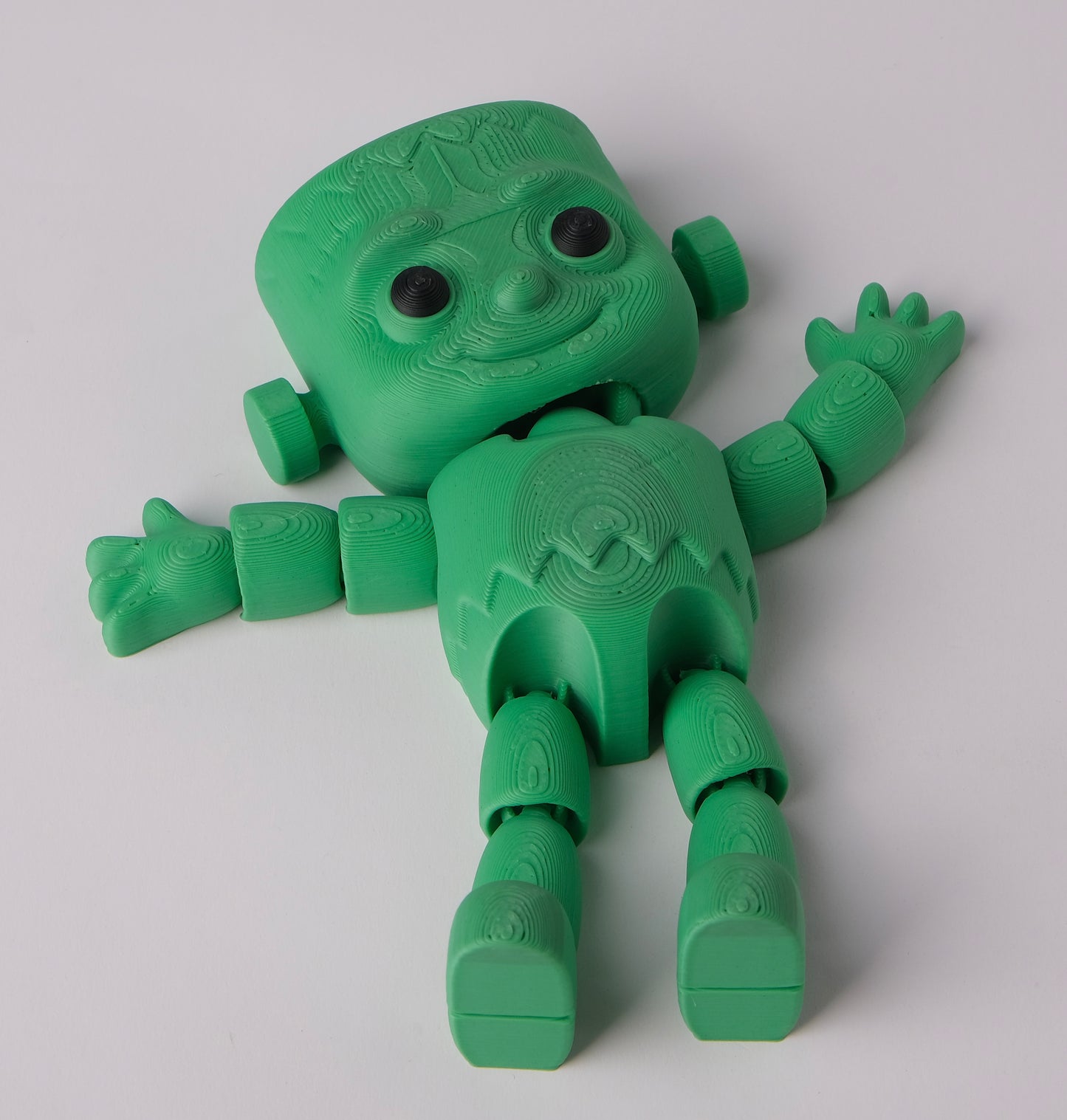 A green 3D-printed articulated toy figure with a blocky, stylized head, textured limbs.