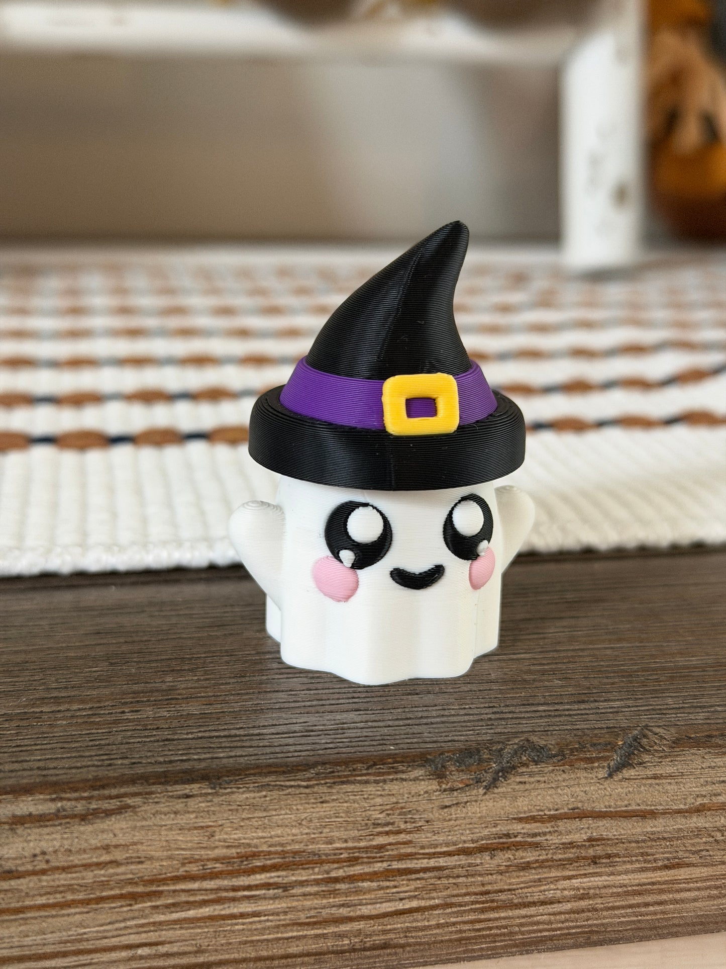Cute ghost figurine with rosy cheeks wearing a black witch hat with a purple band and yellow buckle.