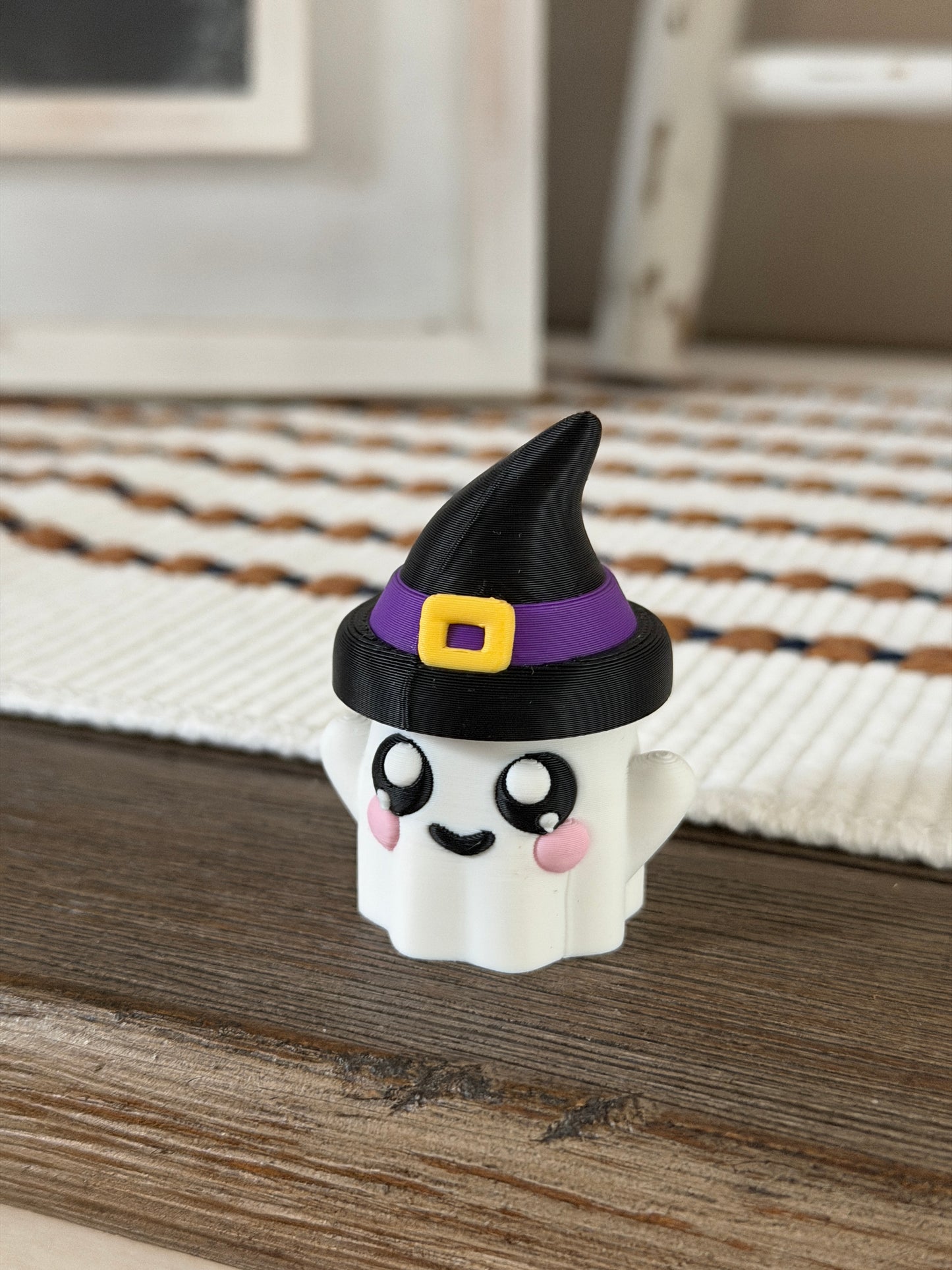Cute ghost figurine with rosy cheeks wearing a black witch hat with a purple band and yellow buckle.