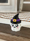 Cute ghost figurine with rosy cheeks wearing a black witch hat with a purple band and yellow buckle.