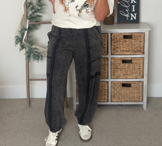 A woman modeling a white graphic t-shirt with a tiger print, paired with dark gray wide-leg cargo pants and white sneakers, standing in a decorated room with a ladder, holiday garland, and a 'Pumpkin' sign.