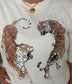 A close-up of a person wearing a white t-shirt with a graphic print of two roaring tigers facing each other. The person is also wearing a gold heart pendant necklace.